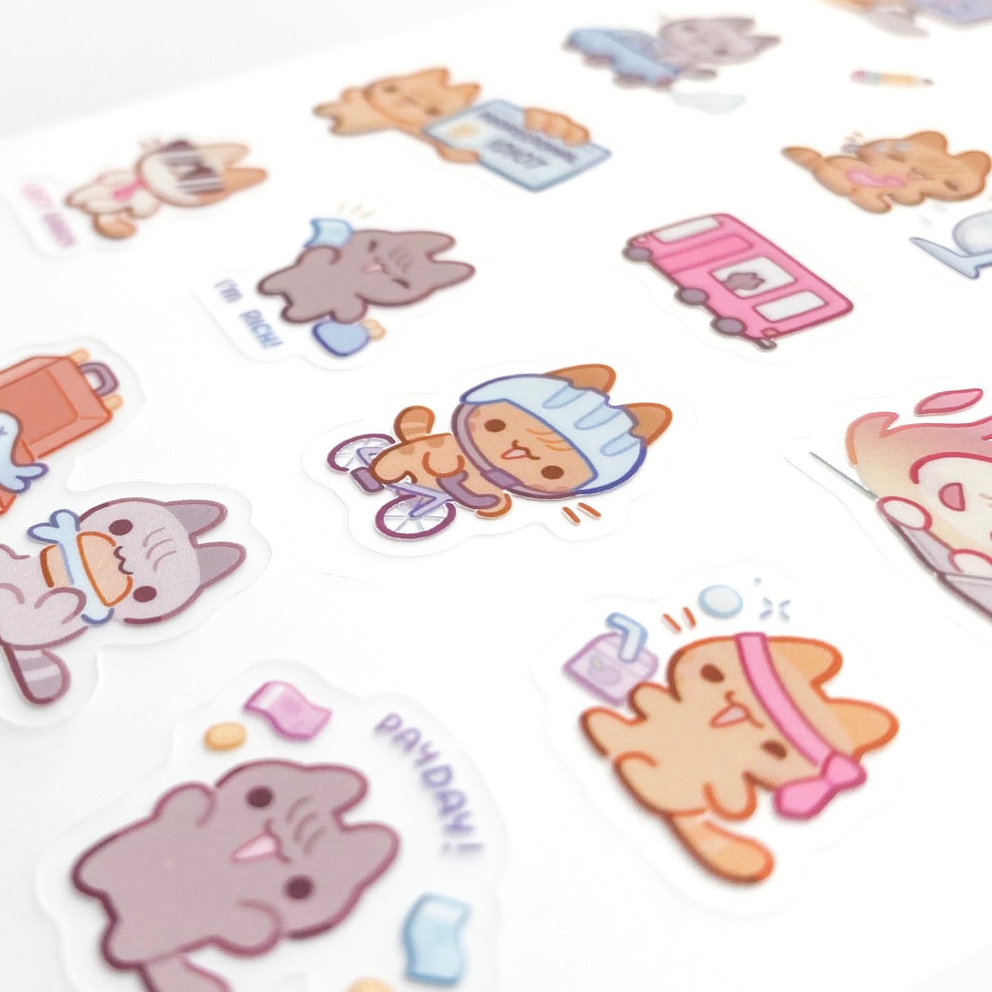 a close-up of the stickers to show the good print quality. In the middle is cat riding a bicile to work. There's also one eating a fish sandwich for lunch! Another is drunk on peach juice and his tie on his head.