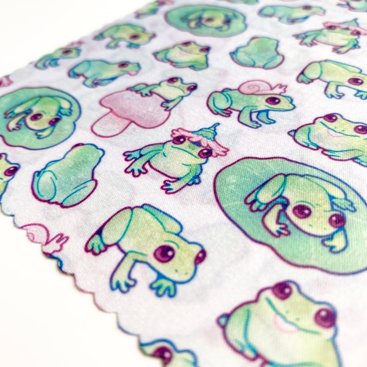 a close-up of the custom printed cloth with a froggie artwork! There's also a snail, a mushroom and a little flower hat. One is sticking out its tongue.