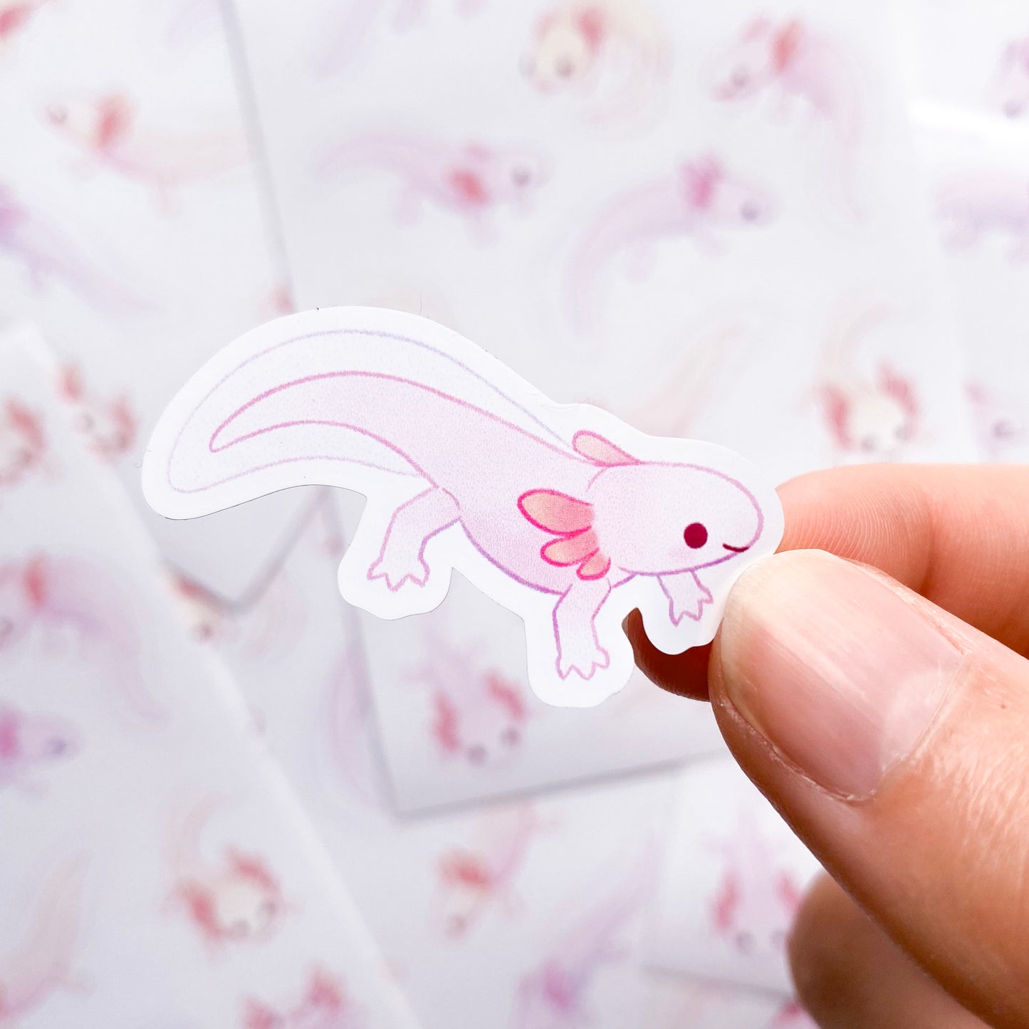 A sticker of a swimming axolotl with its legs stretched out. Each sticker is an individual unique drawing of an axolotl in a different pose. Mexican walking fish don't really do much, so these guys aren't either. They are just chilling happily in the water with lots of silly little faces!