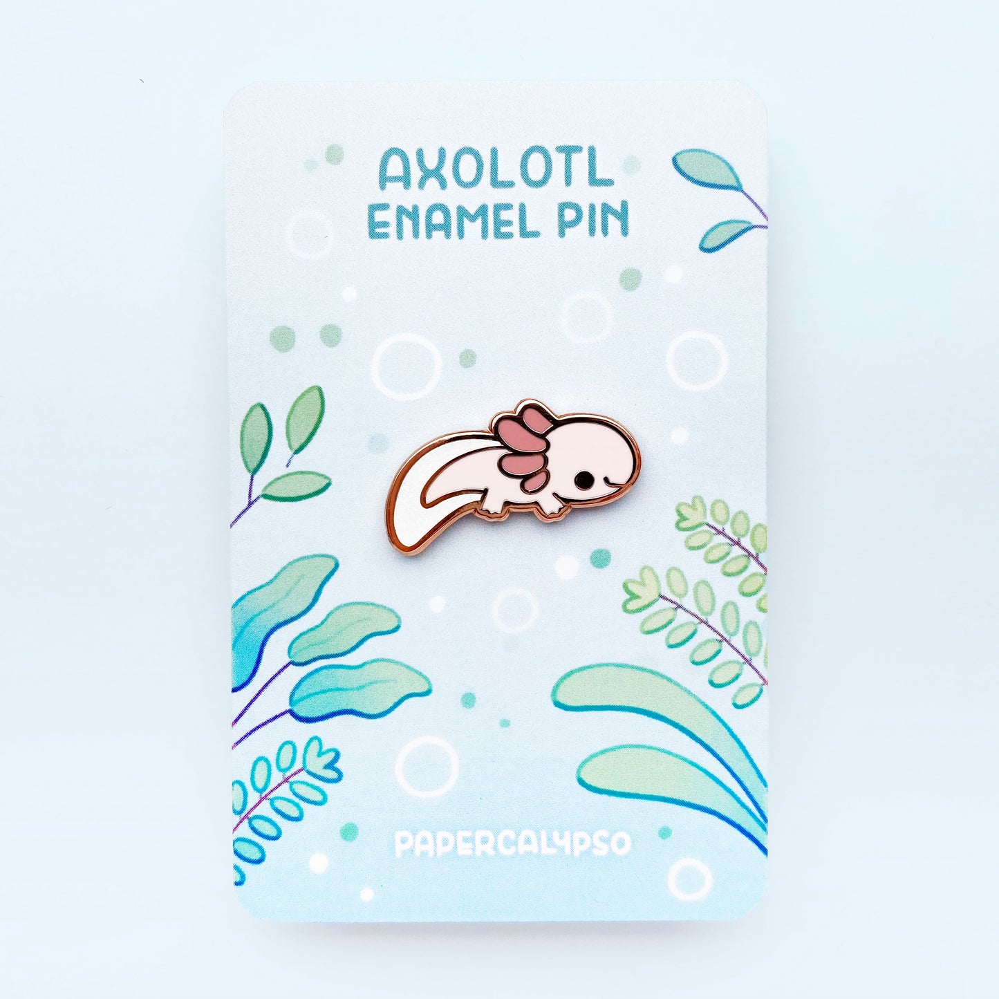 A copper plated hard enamel pin of a pink leucistic mexican axolotl. He has stubby cute little feet and gills. His fin is filled with glitter enamel.