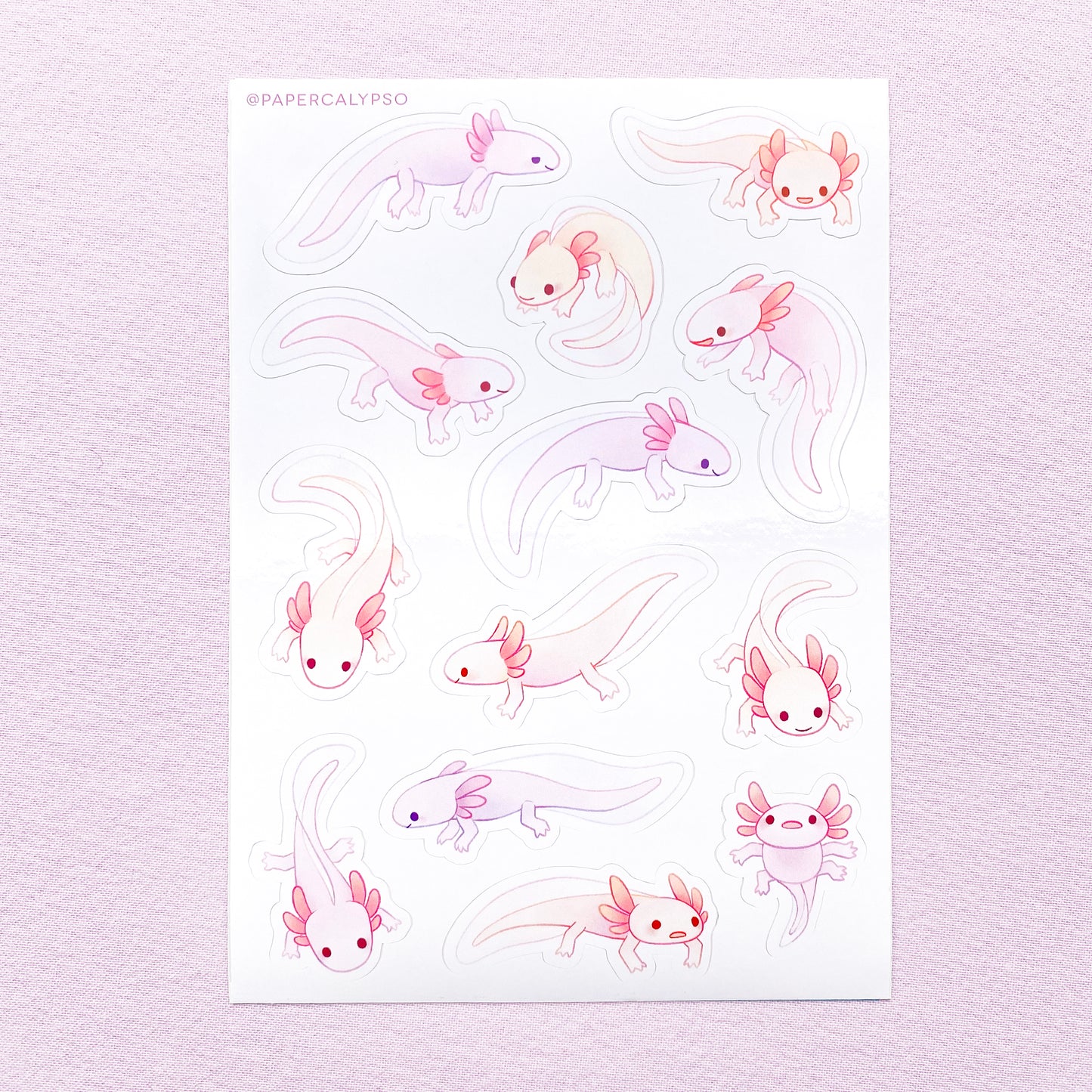 The axolotls are purple, pink and yellow pastel coloured, with little grabby fingers and thick tails. Their gills are stubby, round and cute. Most of them are smiling, while some look a bit stupid and clueless. The sticker sheet has thirteen unique stickers printed on white glossy thin vinyl. This makes them sturdy and waterproof, but not too thick to use in a journal.