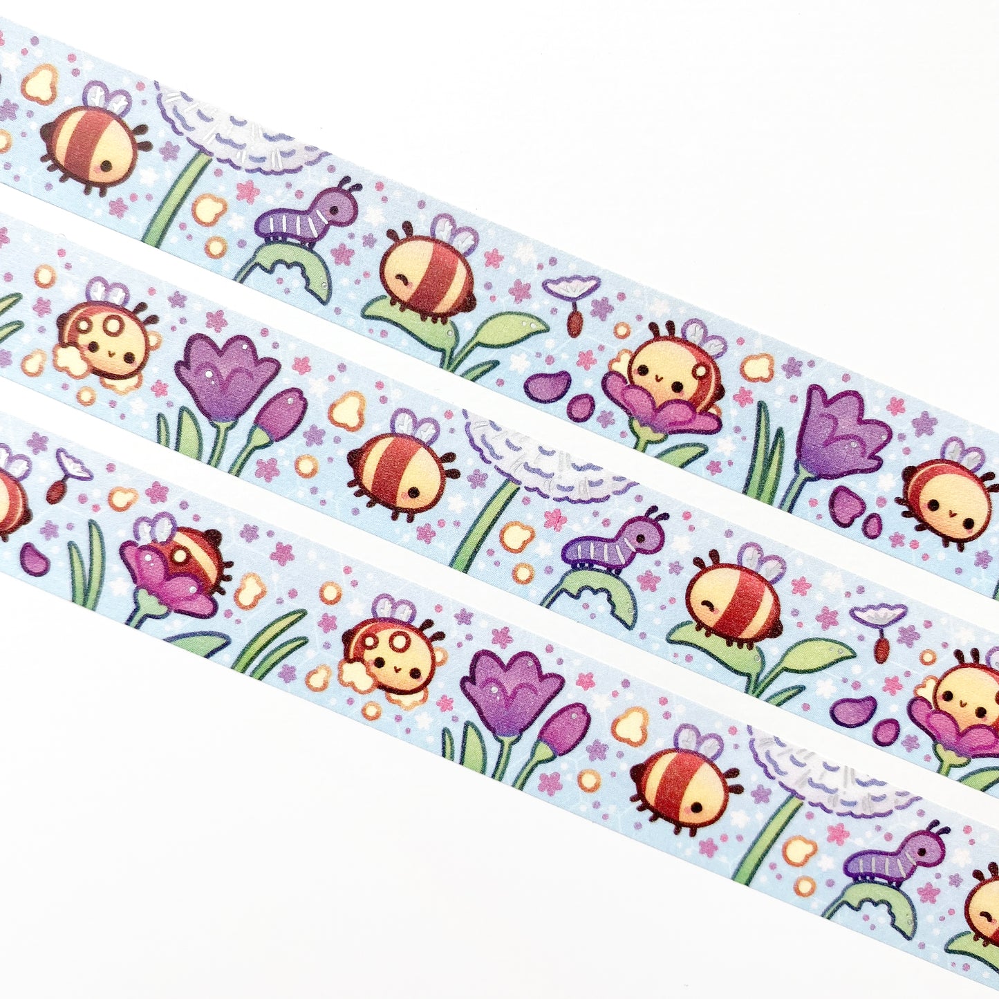 A close-up of the washi tape. The bees are surrounded by petals, pollen, little flowers and dandelion seeds. In the background you can see a faint hexagonal pattern resembling the honeycombs of a bee hive.