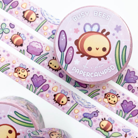 kawaii bee themed washi tape featuring pastel round bees flying in a pink spring meadow with plants. The bees are happily working and collecting pollen among the crocus flowers, dandelions and clovers. One bee is saying hi to a caterpillar!