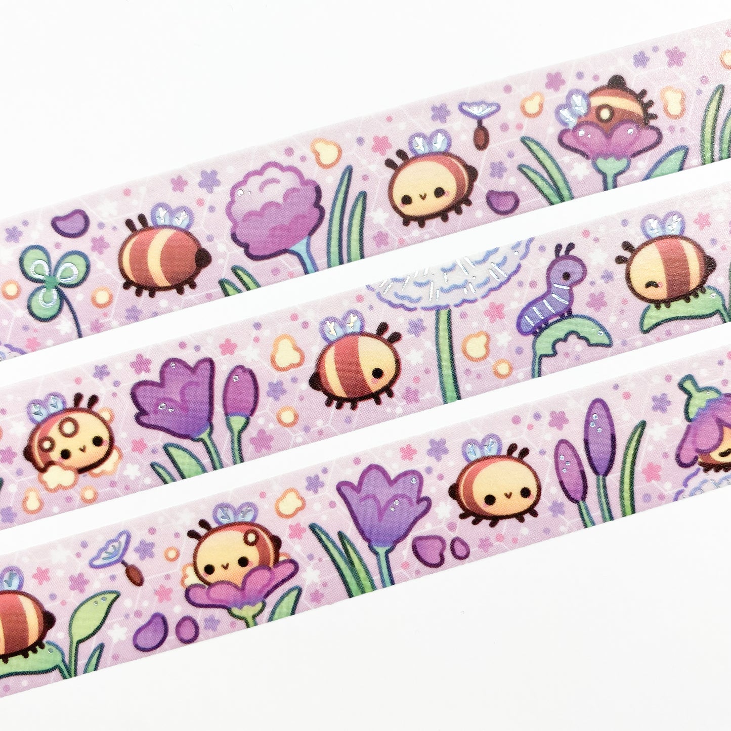 A close-up of the washi tape. The bees are surrounded by petals, pollen, little flowers and dandelion seeds. In the background you can see a faint hexagonal pattern resembling the honeycombs of a bee hive.