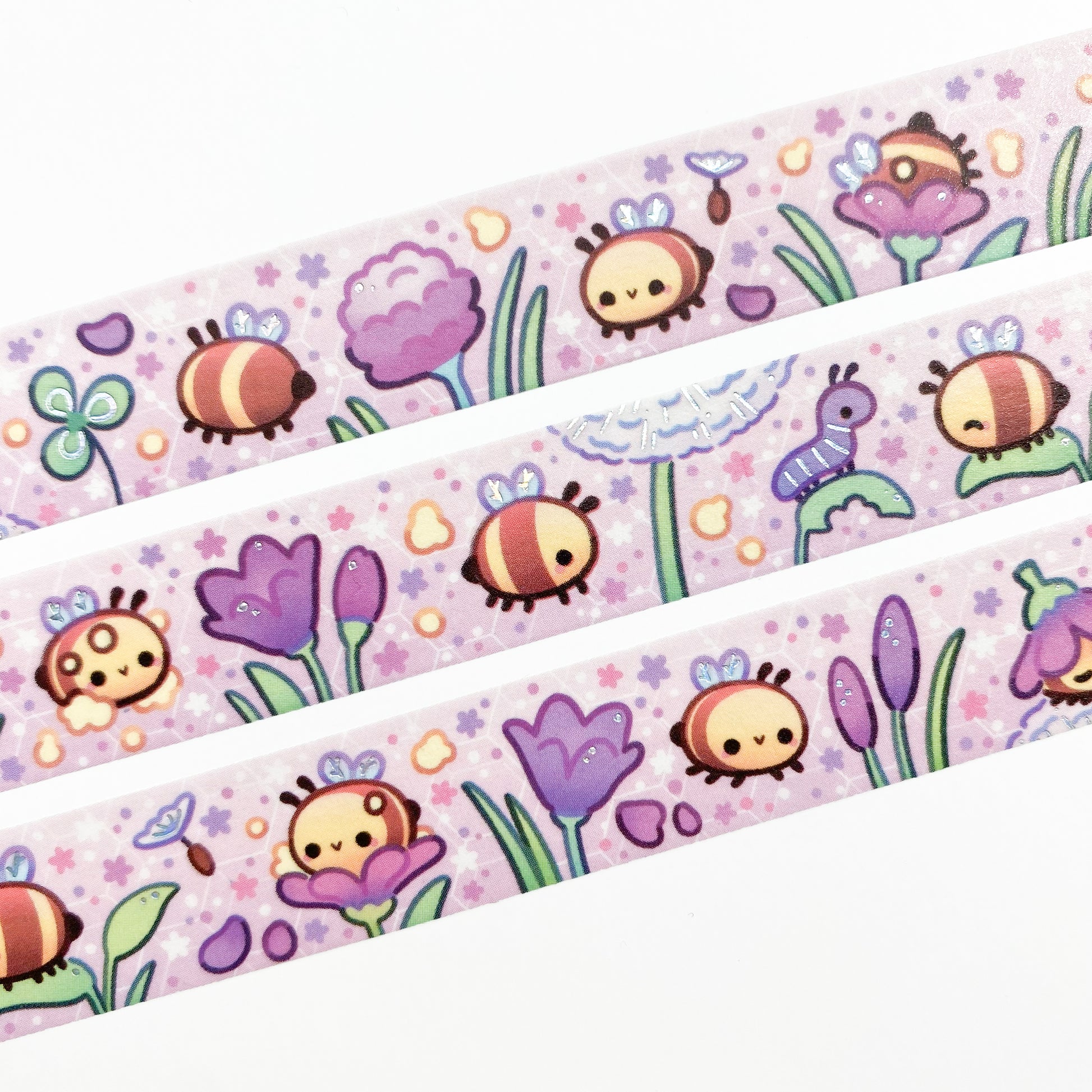 A close-up of the washi tape. The bees are surrounded by petals, pollen, little flowers and dandelion seeds. In the background you can see a faint hexagonal pattern resembling the honeycombs of a bee hive.