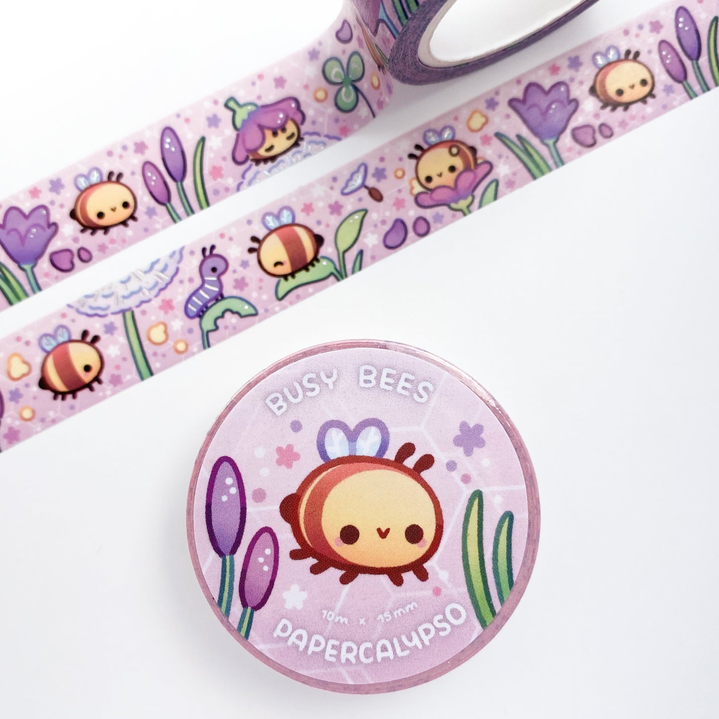 the roll of washi tape is packaged with shrink wrap plastic and a round sticker on one side. On it is an adorable happy bee surrounded by flowers and other plants. It reads "Busy Bees, 10 metres by 15 milimetres, by Papercalypso"