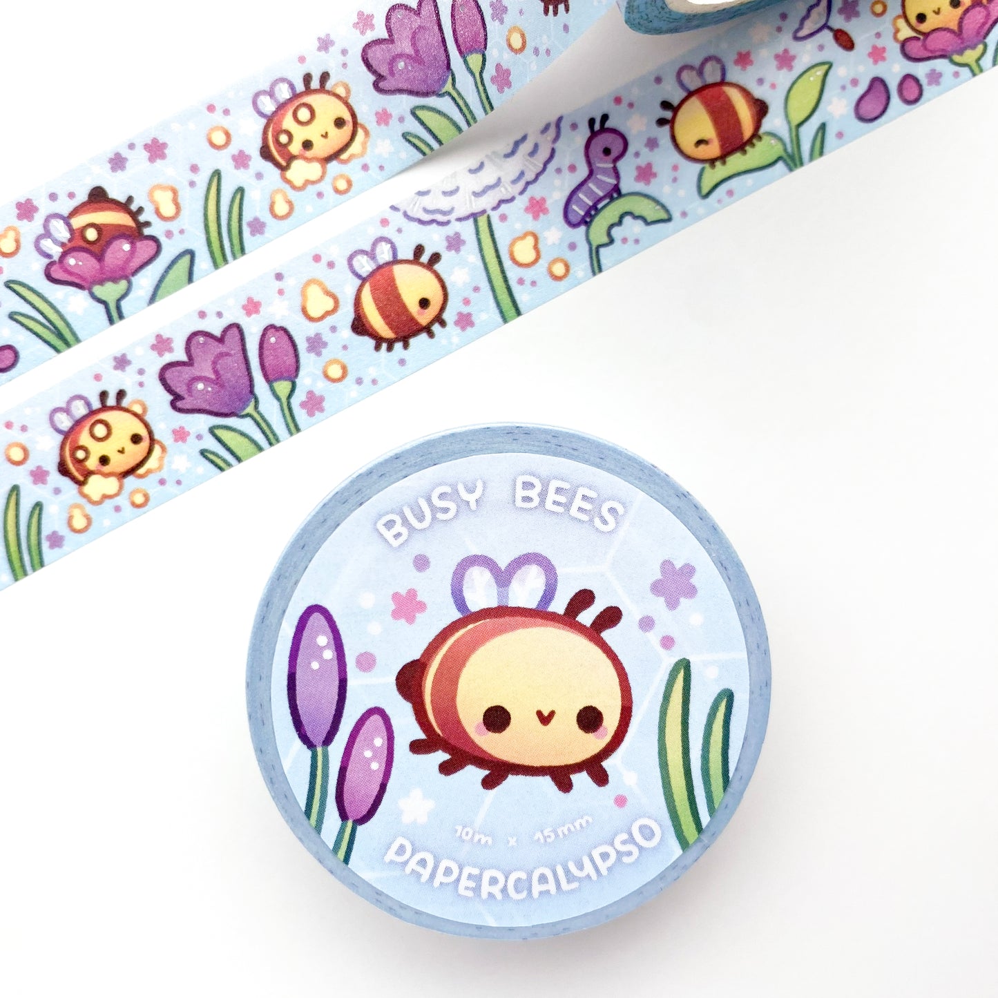 the roll of washi tape is packaged with shrink wrap plastic and a round sticker on one side. On it is an adorable happy bee surrounded by flowers and other plants. It reads "Busy Bees, 10 metres by 15 milimetres, by Papercalypso"