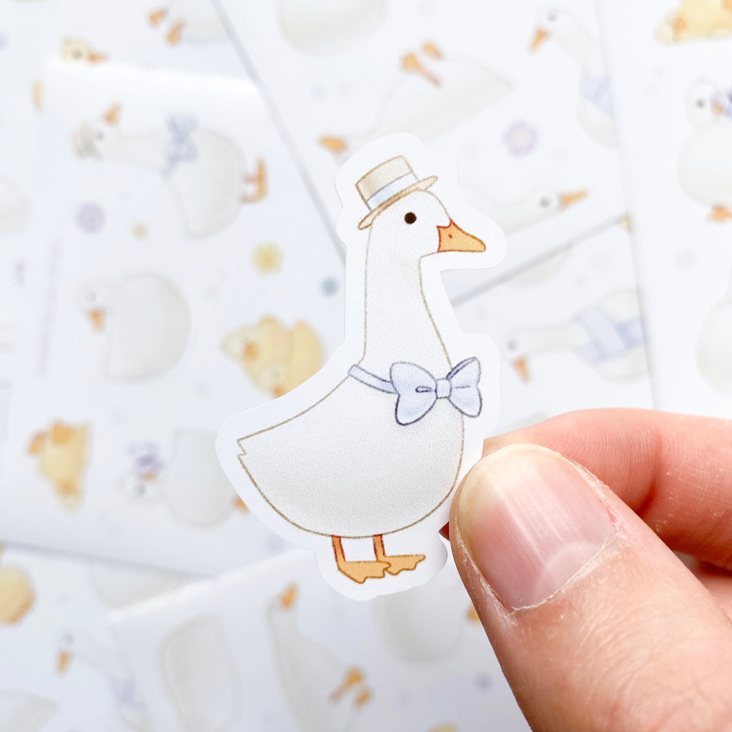 A sticker of of a duck wearing a blue bowtie and a fancy little hat. Each sticker is an individual unique drawing of a duck in a different pose. Many of them are doing silly things, one is wearing a scarf, another is lying on his back, and another has a flower on its head.