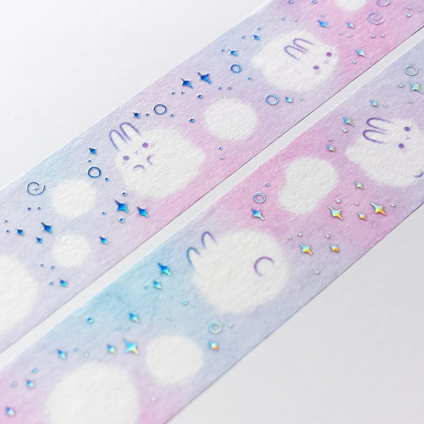 A close-up of the washi tape. The rabbits are surrounded by holographic swirls and sparkles, and smaller, non-sentient balls of white dust.