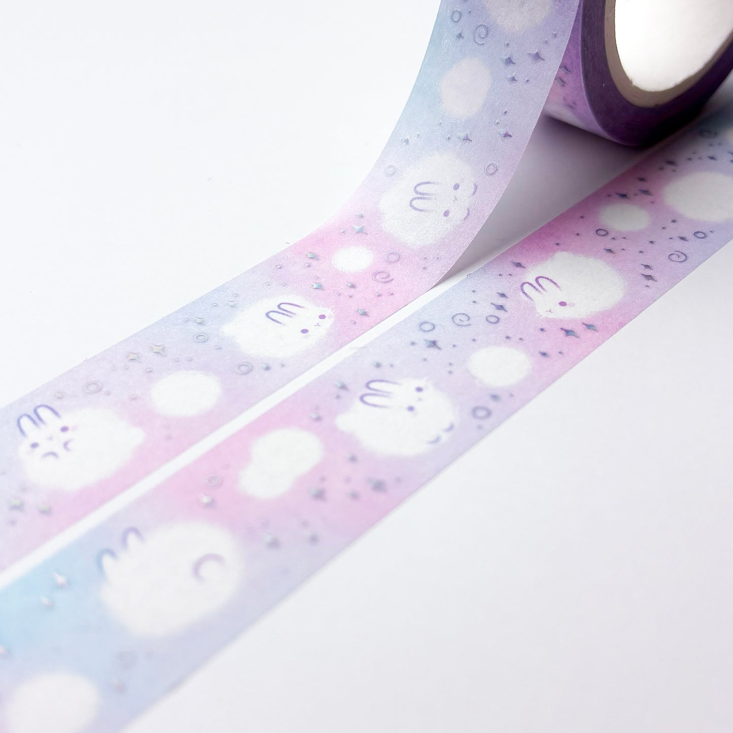 The roll of washi tape is packaged in plastic foil and a round sticker on each side. On it is an adorable fluffy bunny looking at us. It reads "Dust Bunnies, 10 metres by 15 milimetres, by Papercalypso" 
