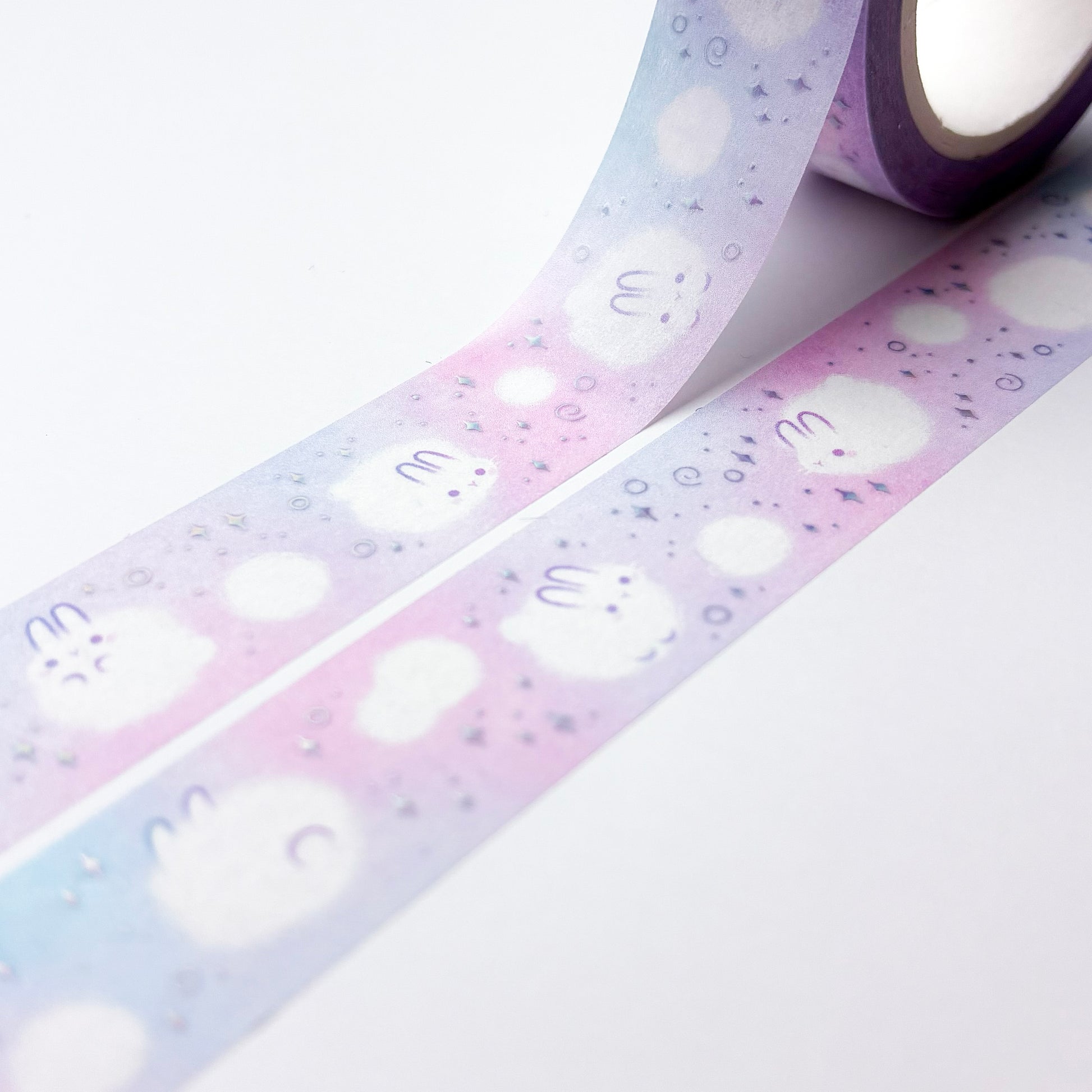 The roll of washi tape is packaged in plastic foil and a round sticker on each side. On it is an adorable fluffy bunny looking at us. It reads "Dust Bunnies, 10 metres by 15 milimetres, by Papercalypso" 