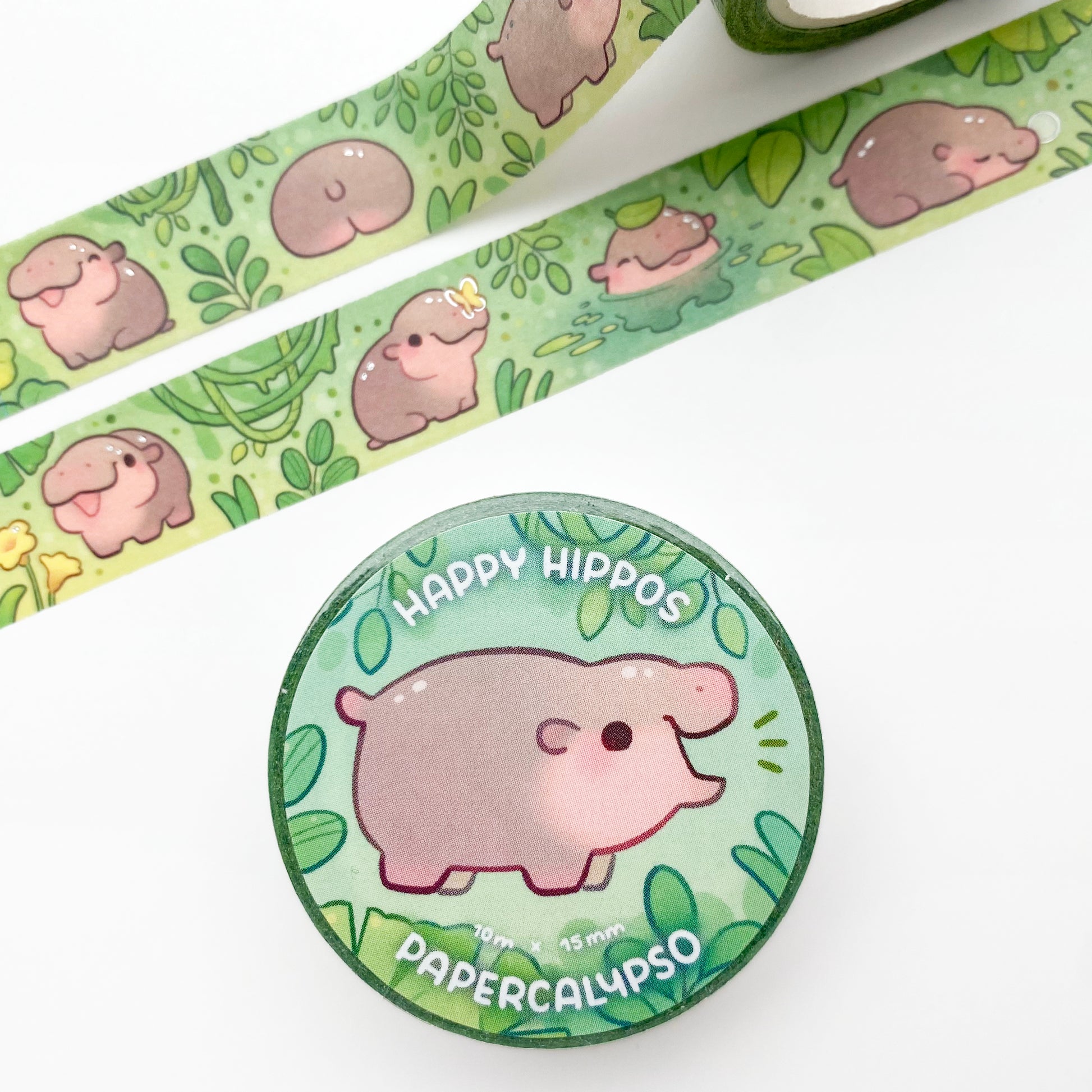 the roll of washi tape is packaged with shrink wrap plastic and a round sticker on one side. On it is an adorable baby hippo surrounded by leaves. It reads "Happy hippos, 10 metres by 15 milimetres, by Papercalypso"