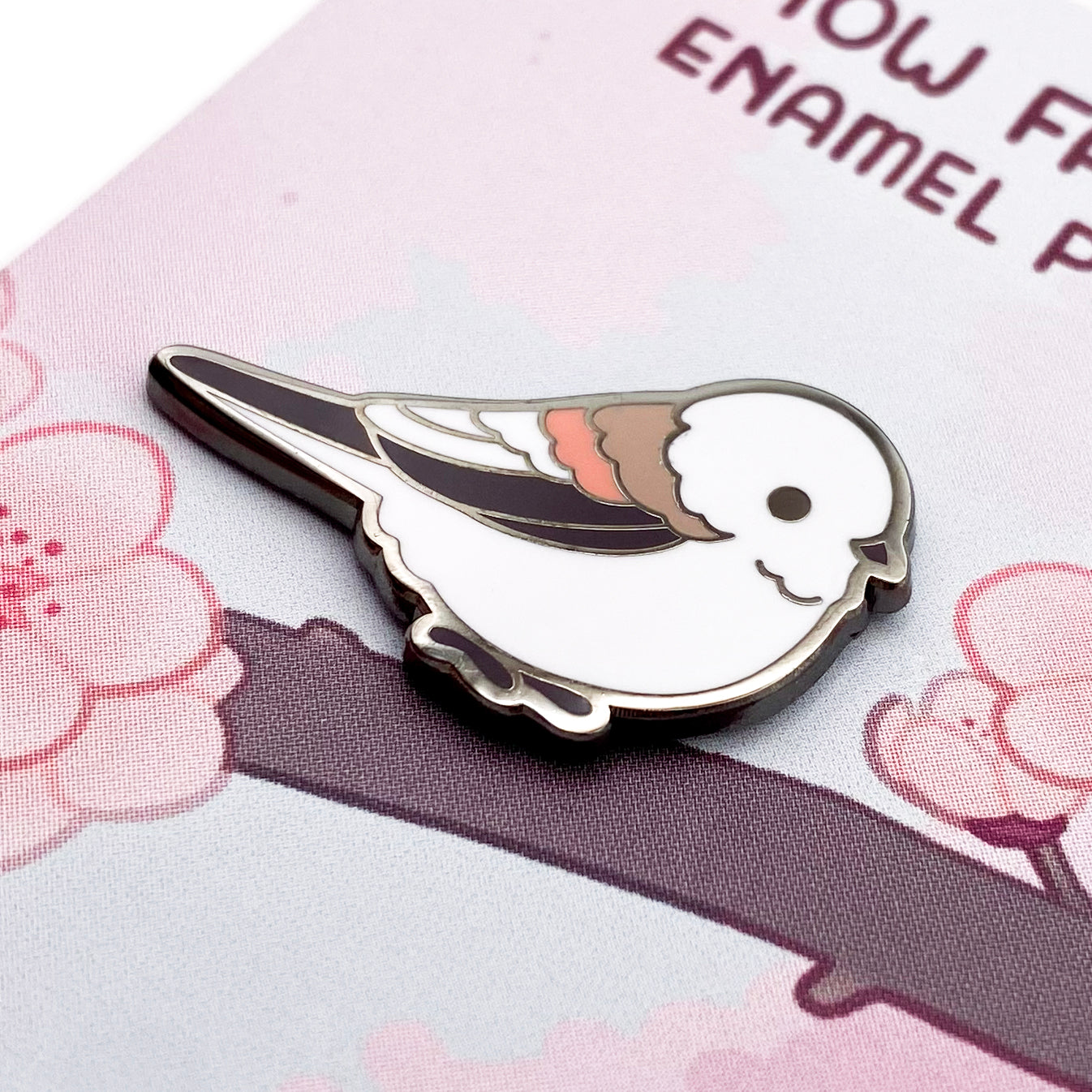 A close-up of the pin so you can see the details. The pin backing is a branch of blooming cherry blossoms with the title "Snow Fairy Enamel Pin."