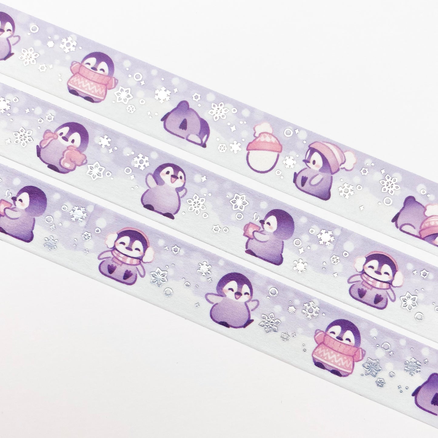 A close-up of the washi tape. The baby penguins are surrounded by large snowflakes falling from the sky. They're all having fun in the snow, and blushing in the cold. One penguin is drinking a hot chocolate.