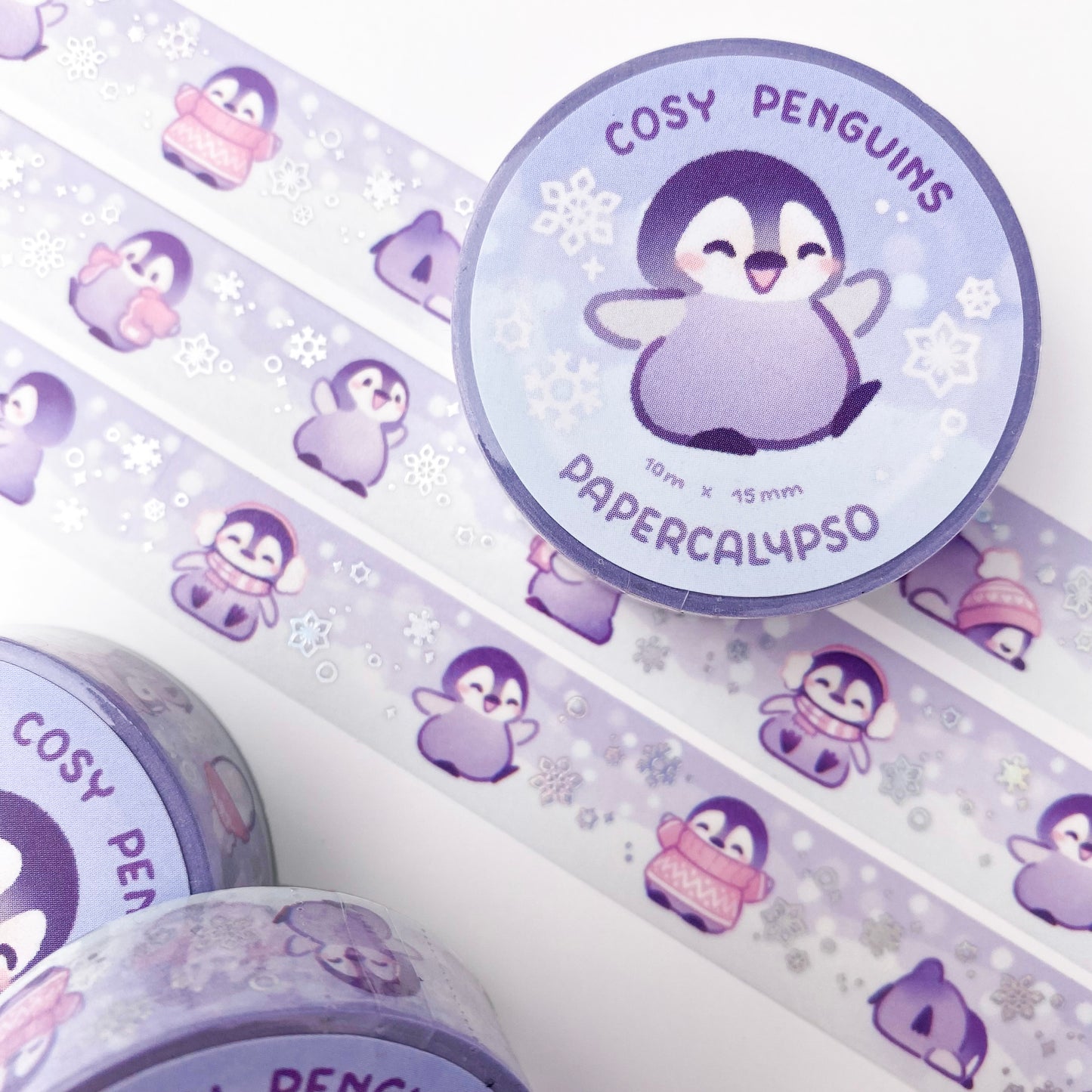 kawaii penguin themed washi tape featuring adorable cartoon baby penguins in a pastel winter wonderland. The penguin chicks are waddling around in pink winter clothing like hats, puffer jackets, earmuffs and scarves.