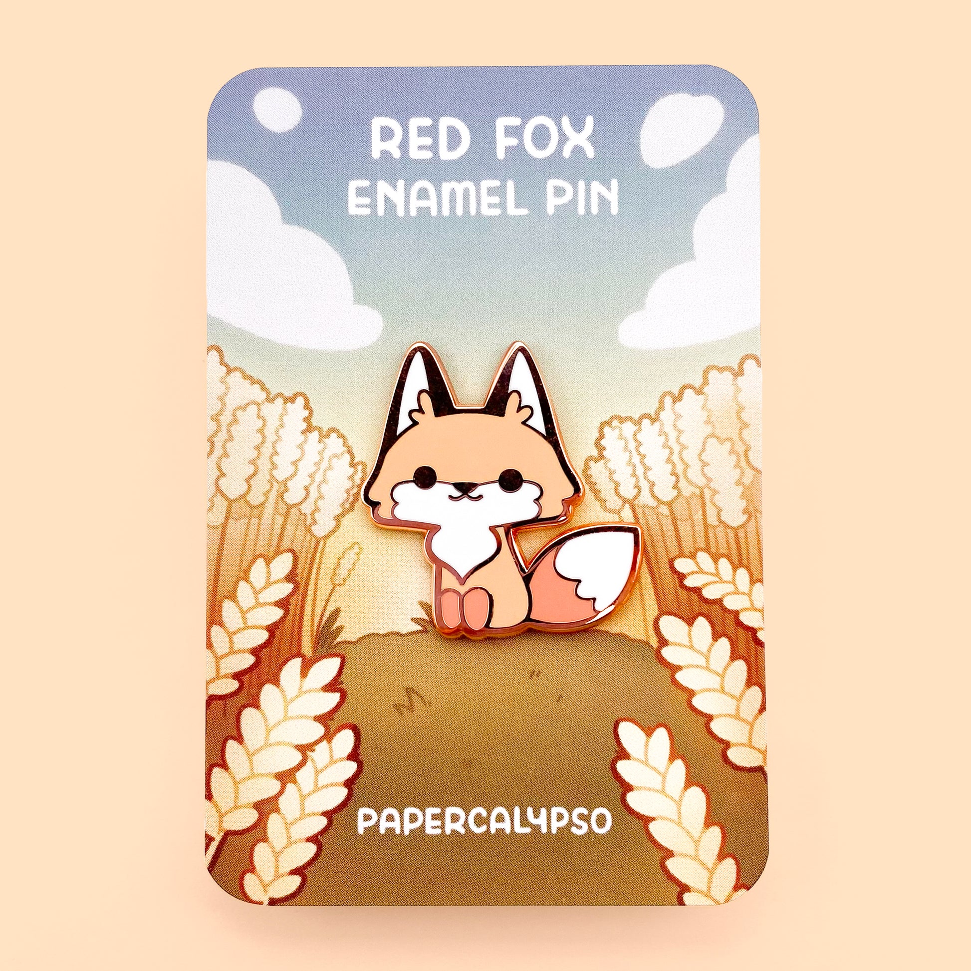A copper plated hard enamel pin of a happy cartoon red fox sitting and smiling. He's very kawaii and cute and has a big fluffy tail.