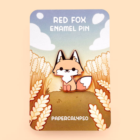 A copper plated hard enamel pin of a happy cartoon red fox sitting and smiling. He's very kawaii and cute and has a big fluffy tail.