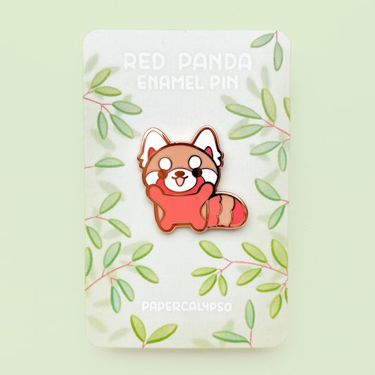 A copper plated hard enamel pin of a red panda baby holding up its paws. He's red and orange with a kawaii stylisation.