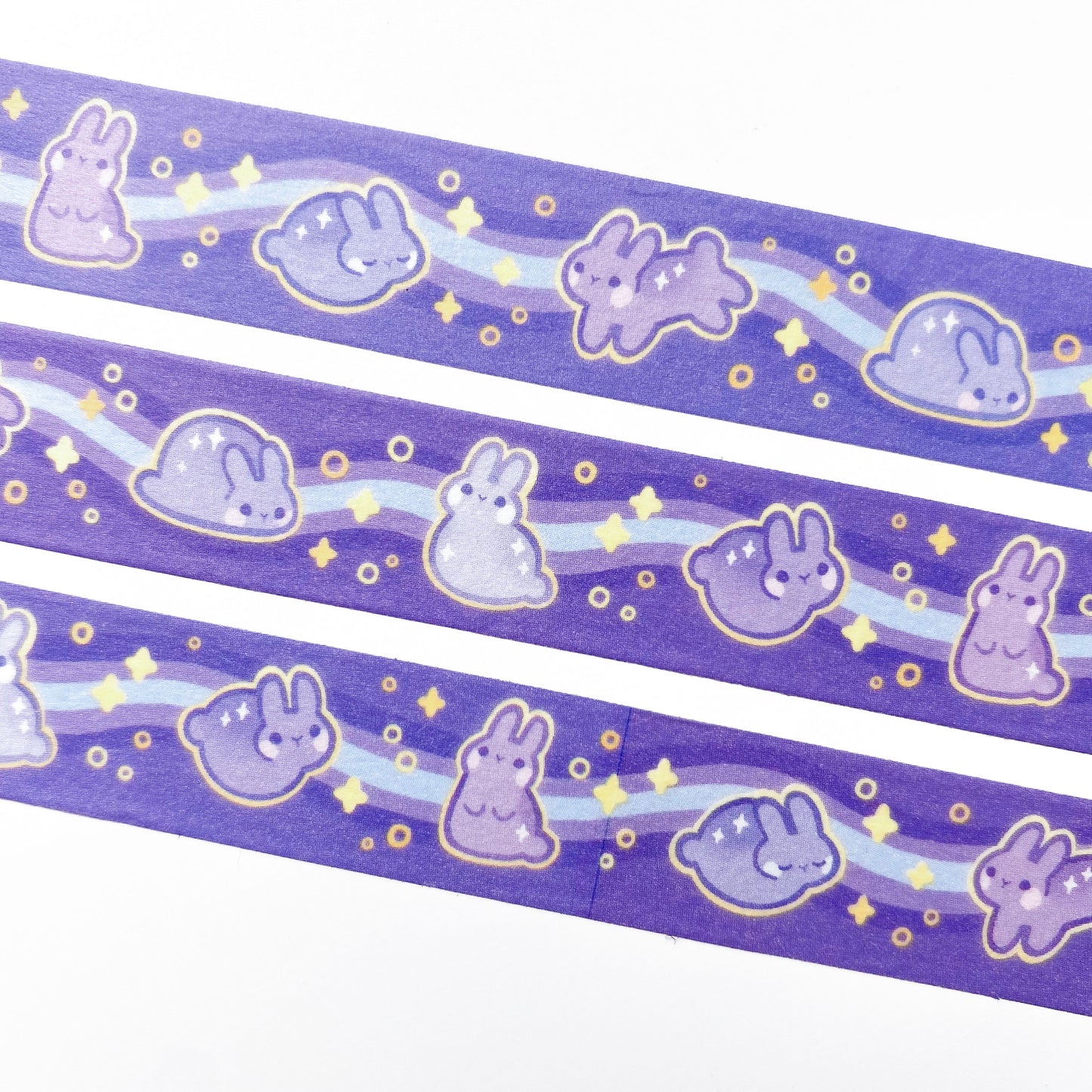 A close-up of the washi tape. The rabbits are surrounded by glowing yellow stars and circles. In the background is a blue and purple wavy line.