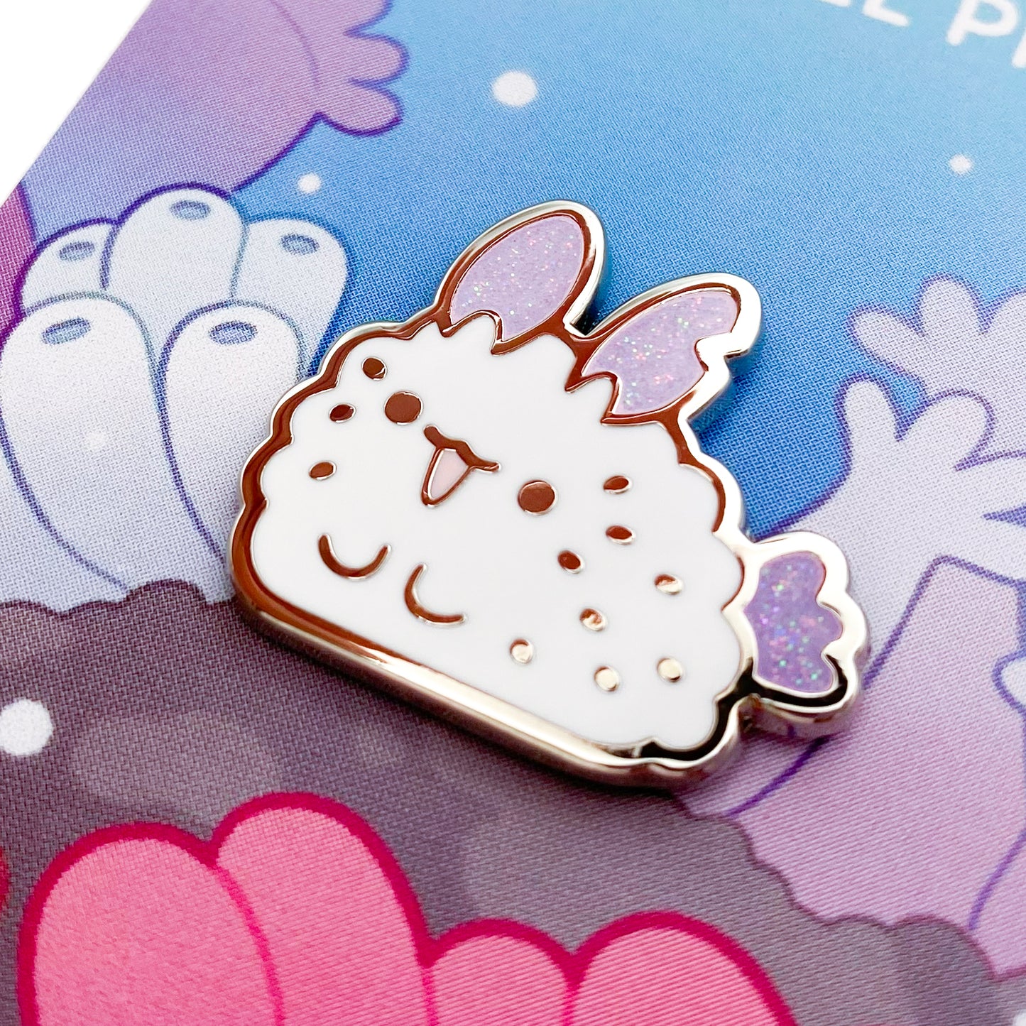A close-up of the cute pin. The glitter accents sparkle in the light. The pin backing is a coral reef with the title "Sea Bunny Enamel Pin."