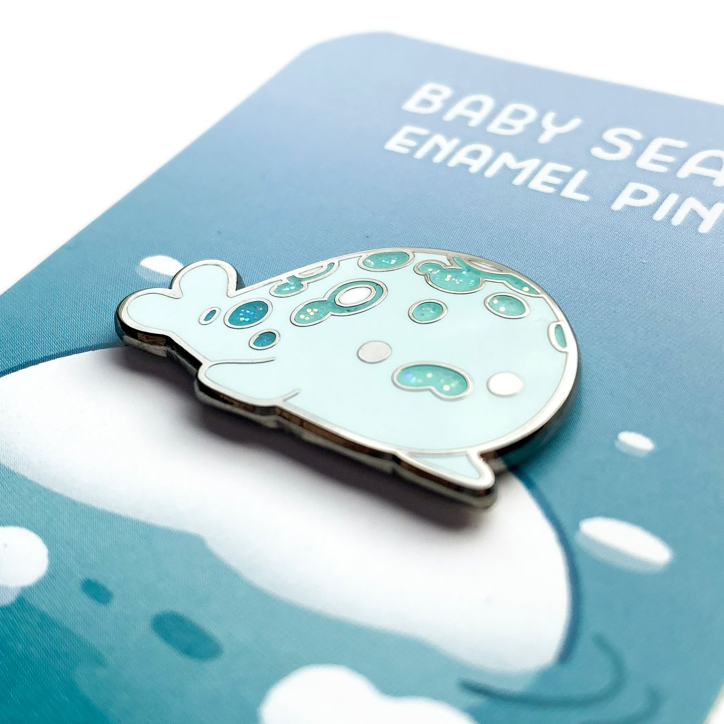 A close-up of the pin so you can see the details. The glitter accents sparkle in the light.  The pin backing features an iceberg in the sea, on which the seal is sitting.