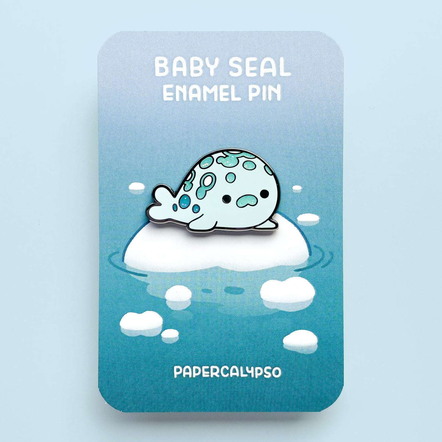 A black nickel hard enamel pin of a little spotted harbor seal. He's so fat, he's almost a circle. He's looking at you with a cute face!