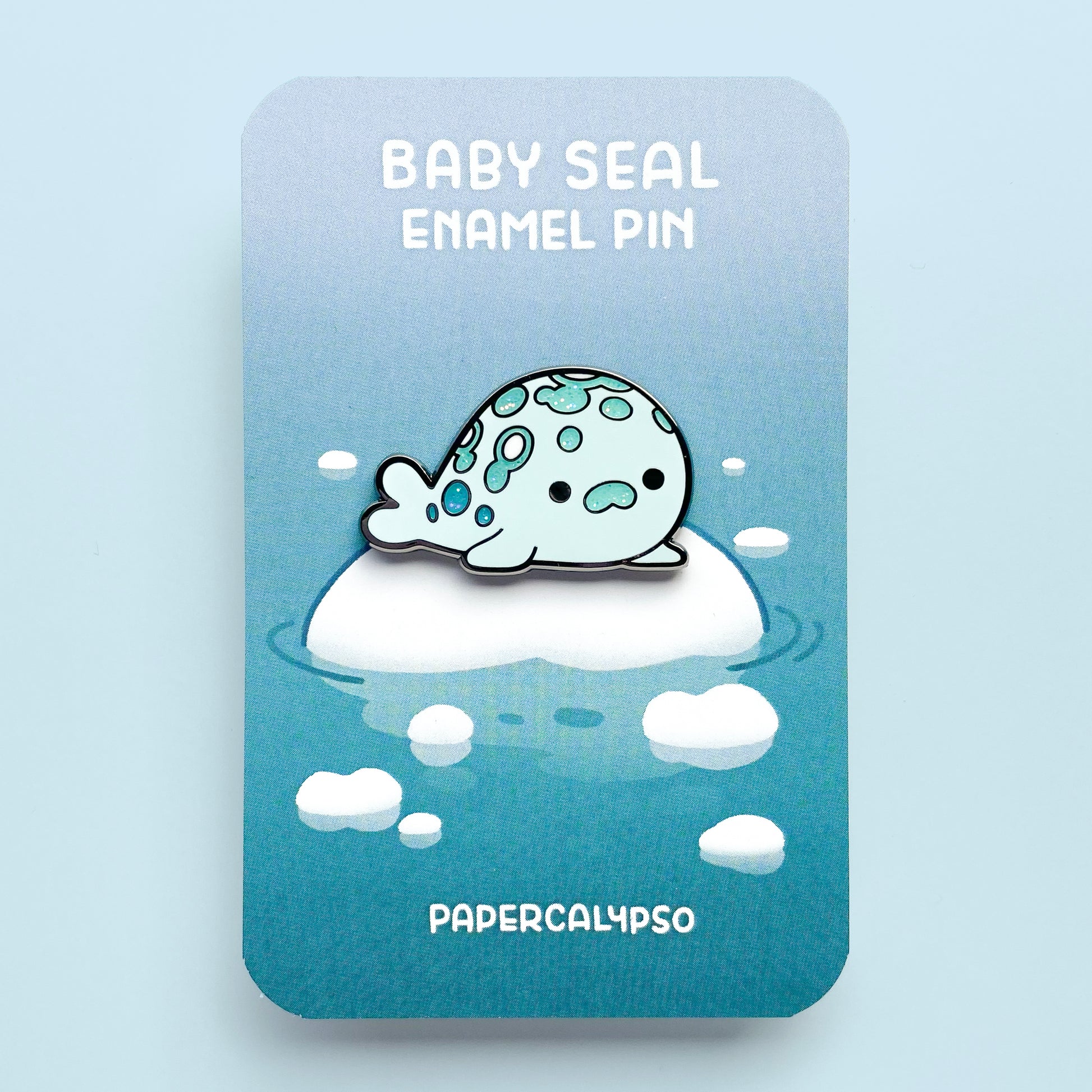 A black nickel hard enamel pin of a little spotted harbor seal. He's so fat, he's almost a circle. He's looking at you with a cute face!