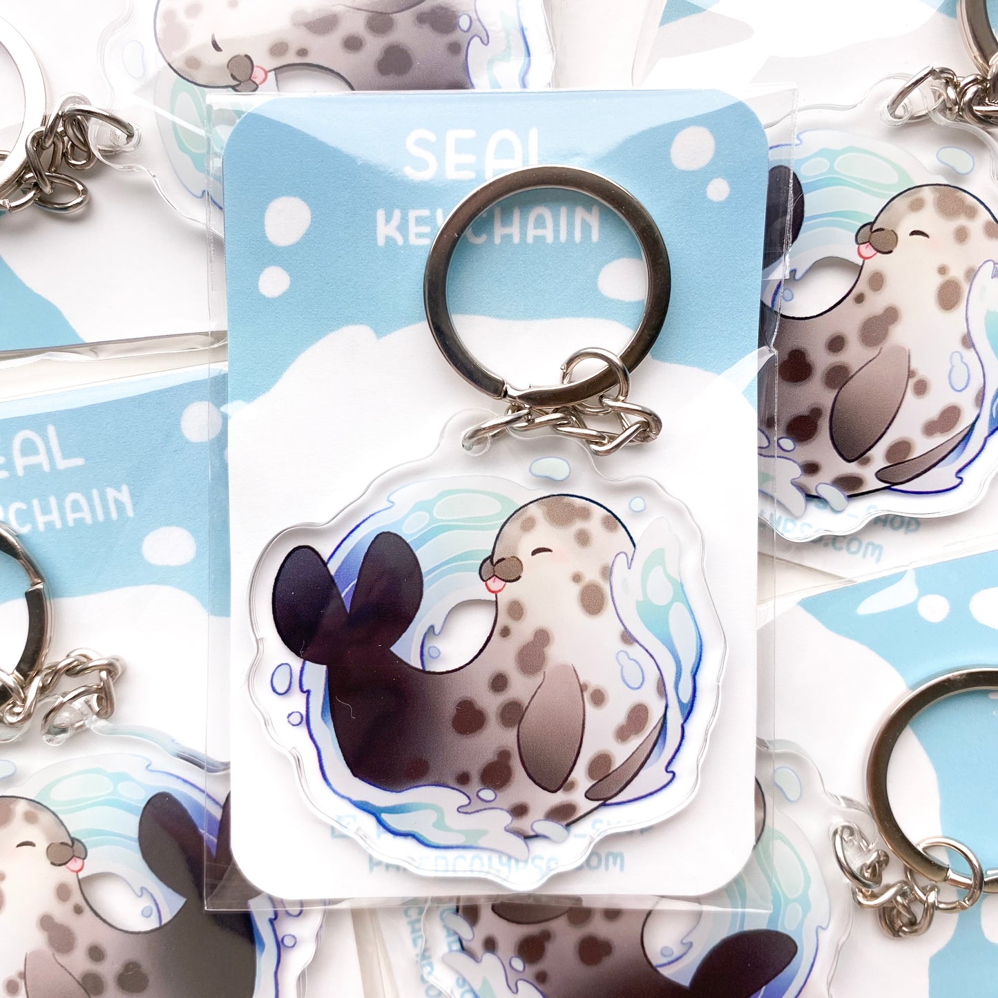 the keychain is packaged in a cellophane baggie with a printed blue wave themed backing. The chain is a round silver keyring.