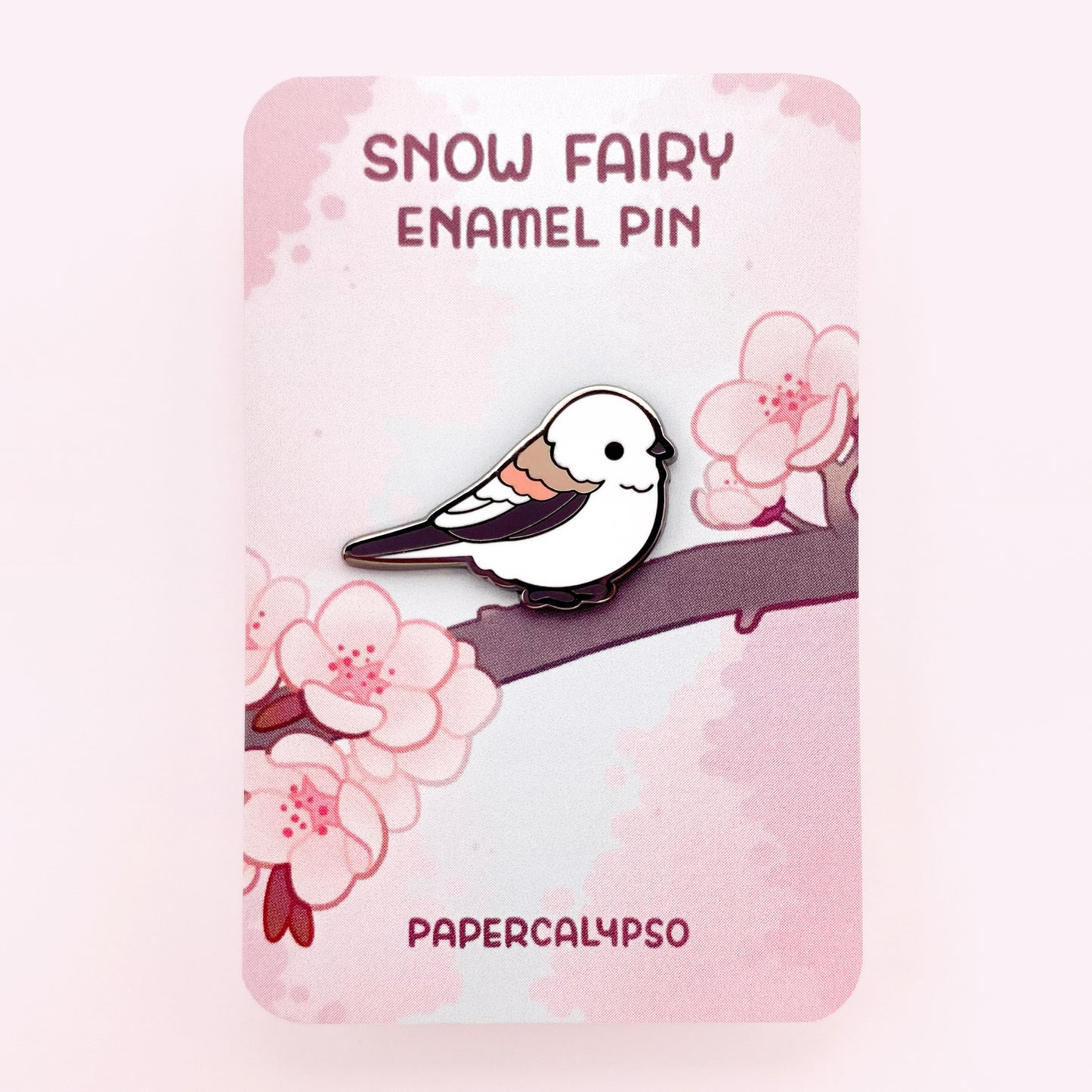 Snow fairy black nickel enamel pin on a backing card with Japanese pink cherry blossoms.
