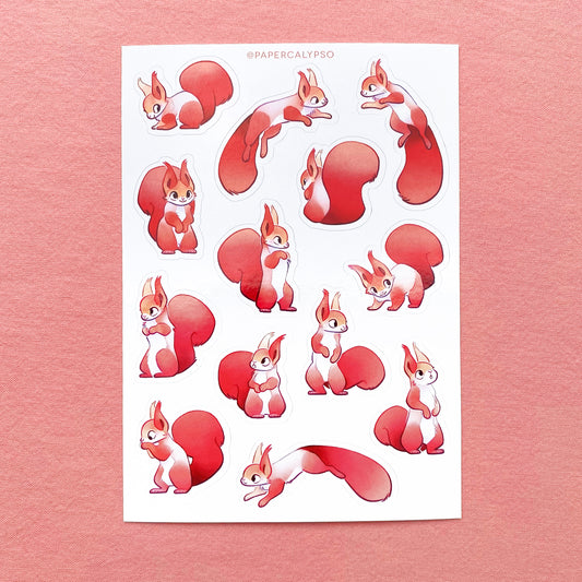 The squirrels are red european squirrels with big fluffy tails and tufted ears. They have rounded cartoon shapes and big eyes, so they appear cute. They are in their winter coat, their bodies have thicker greyish fur. The sticker sheet has thirteen unique stickers printed on white matte thin vinyl. This makes them sturdy and waterproof, but not too thick to use in a journal.