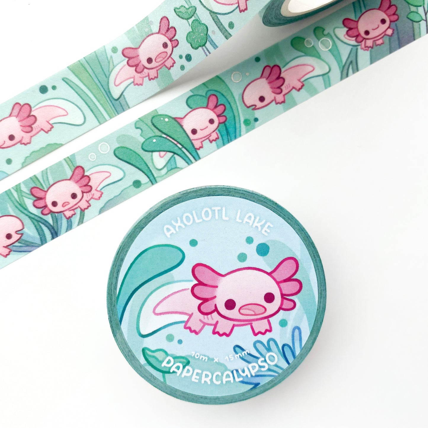 the roll of washi tape is packaged with shrink wrap plastic and a round sticker on one side. On it is an adorable axolotl surrounded by underwater plants. It reads "Axolotl Lake, 10 metres by 15 milimetres, by Papercalypso"