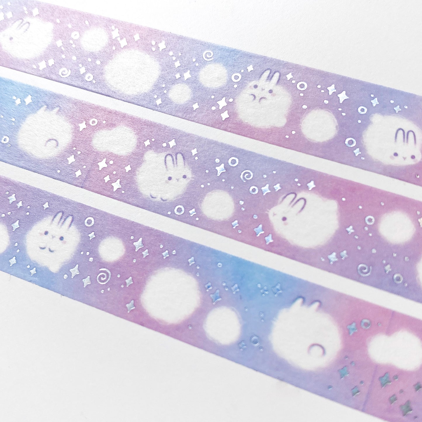 A close-up of the washi tape. The rabbits are surrounded by silver foil swirls and sparkles, and smaller, non-sentient balls of white dust.