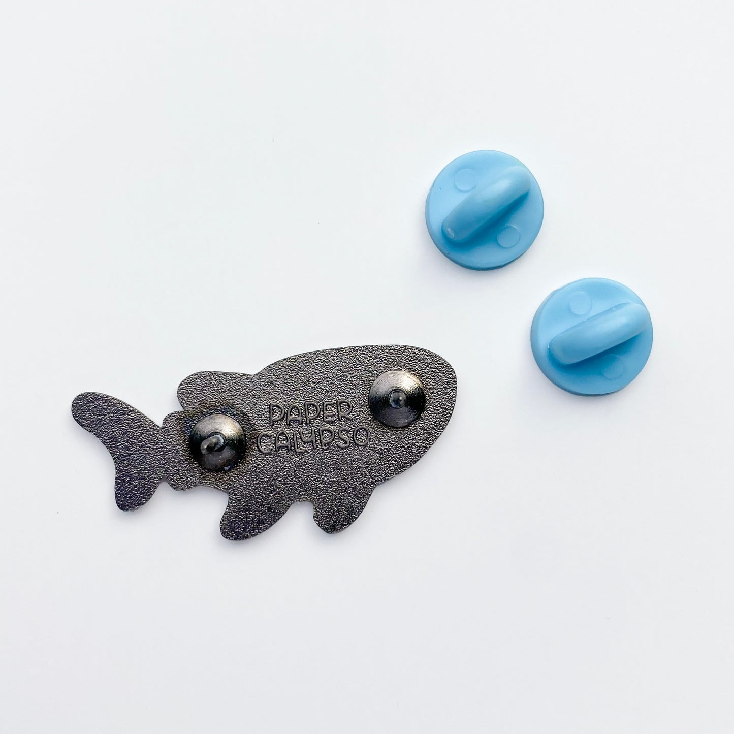 there are two pins on the back for extra security! This way you won't lose your pin if you put it on your clothes or bag. It comes with blue rubber clasps. The back of the pin has a stamp with my watermark and reads "Paper Calypso"